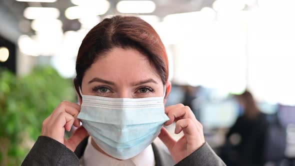 Happy Woman in a Business Suit Walks Through the Office and Takes Off Protective Mask