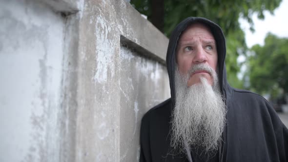 Serious Mature Bald Bearded Man with Hoodie Thinking Against Concrete Wall Outdoors