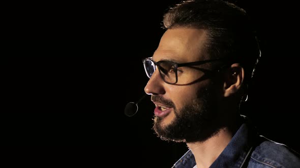 Portrait of a Young Male Business Coach Speaking Through a Microphone in a Dark Conference Room