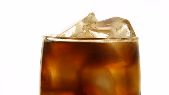 Pouring cola in drinking glass with ice cubes over white
