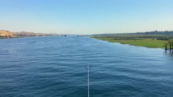 Front of cruise sailing on Nile River between land and plants. Blue sky summer day