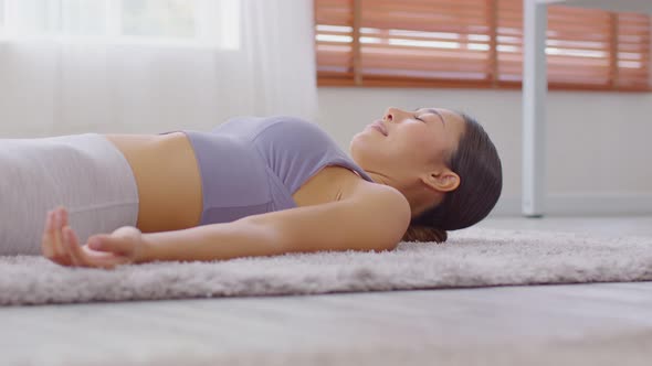 Calm of Asian woman practice yoga Dead Body or Savasana pose with meditation smile at home