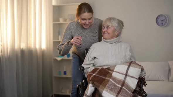 Female Volunteer Gently Covering With Plaid Old Handicapped Woman