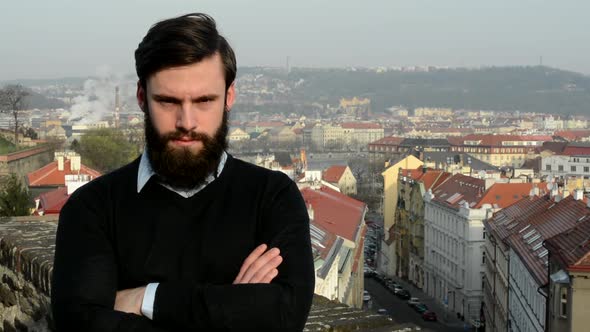 Young Handsome Man with Full-beard (Hipster) Looks To Camera (Confident Look) - City in Background