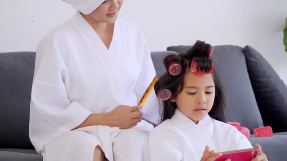 Mother with little daughter in bathrobes doing beauty treatment together at home.