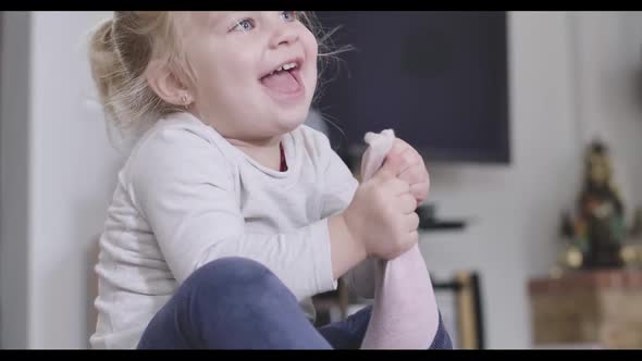 Close-up Portrait of Positive Little Girl Taking Off Pink Sock. Blond Caucasian Child Enjoying Free
