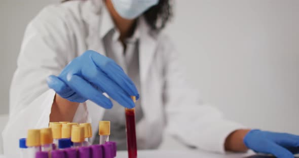 Video of biracial female doctor holding test tube and using laptop on blue background