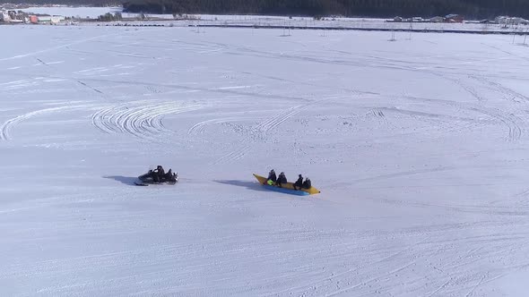 Aerial View Happy people enjoying banana boat ride tied to a snowmobile