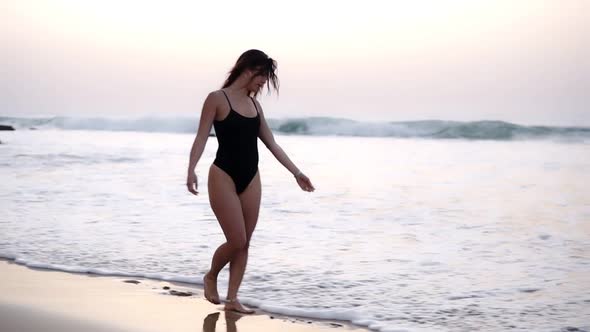 Sexy Girl in a Bathing Black Suit Walks Over a Sandy Beach at the Ocean Gorgeous Long Haired