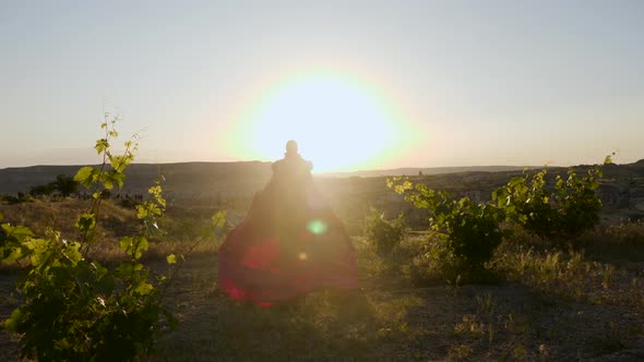 Young Woman Runs in a Long Purple Dress Through a Vineyard on a Mountain