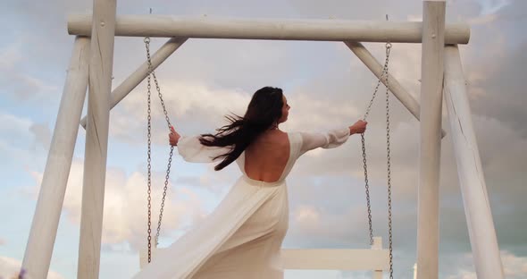 a Gentle Girl in a White Light Dress is Swinging on a Swing