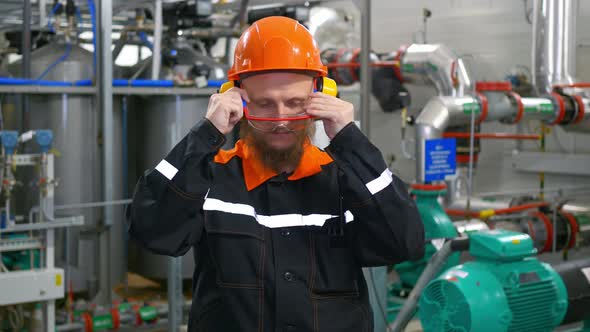 An Experienced Operator in an Orange Hard Hat and Ear Protectors Puts on Safety Goggles Before