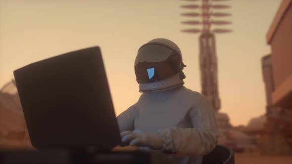 Astronaut in the Space Suit Works on a Laptop in a Space Colony on One of the Planets
