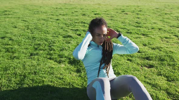 African american woman in sportswear doing sit ups in park