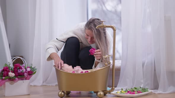 Wide Shot Happy Mother with Rose in Hand Talking to Baby Daughter Lying in Golden Bath with Red