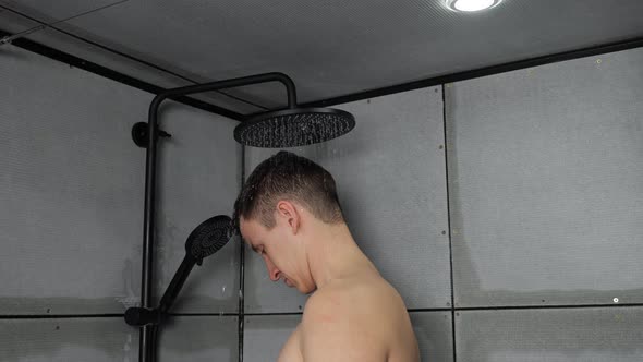 Young Man Takes Shower Washing Hair Under Cold Water at Home