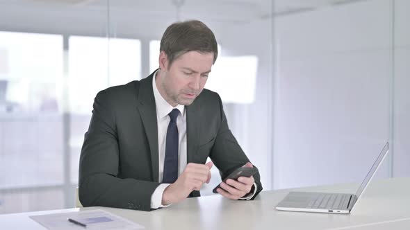 Disappointed Middle Aged Businessman Reacting To Failure on Smartphone 