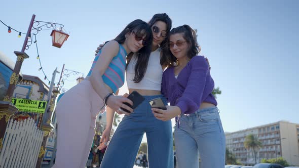 Young Women in Sunglasses Take Selfies with Phones Ground View