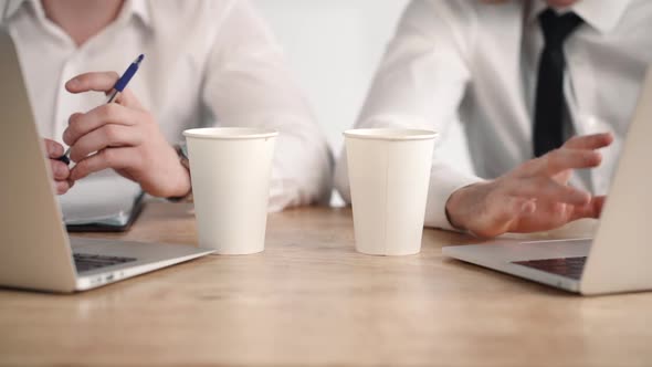 Two Business Men Working Together at Laptops. Computer, Hands and Coffee Cup Closeup. Colleagues