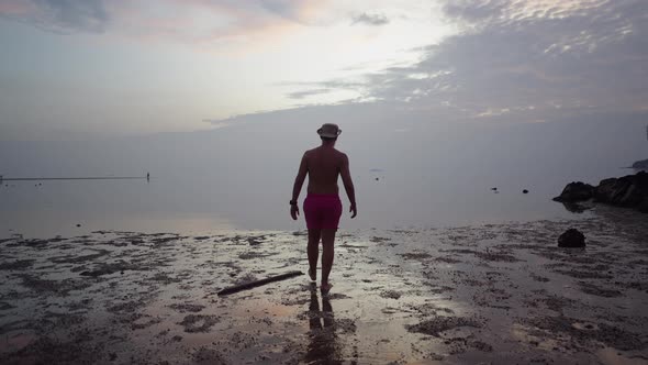 Back View of Silhouetted Man Traveler Walking Towards the Sea Enjoying Seaside Dramatic Sunset