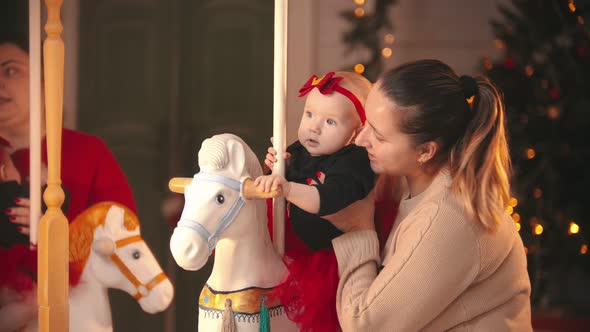 Christmas Concept - Smiling Mother in Beige Sweater with Her Baby in Christmas Studio