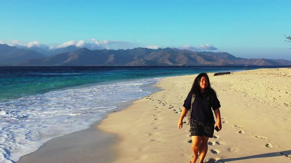 Pretty smiling girl on photoshoot in the sun on the beach on sunny blue and white sand background 4K