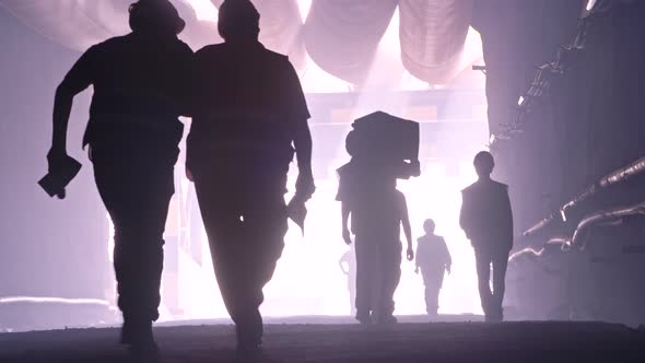 silhouette of many construction workers walking out from a large tunnel