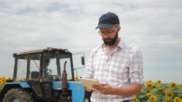 Farmer Uses Tablet in the Field Near the Tractor