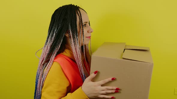 Young Woman in Vest with Cardboard Box on Yellow Background in Studio