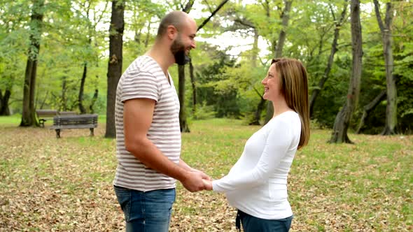 Handsome Man and Young Happy Pregnant Woman Talk Together and Holding Hands in Park