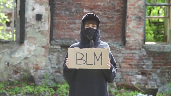 Young Woman Covering Face With Bandana Holding BLM Cardboard And Protesting