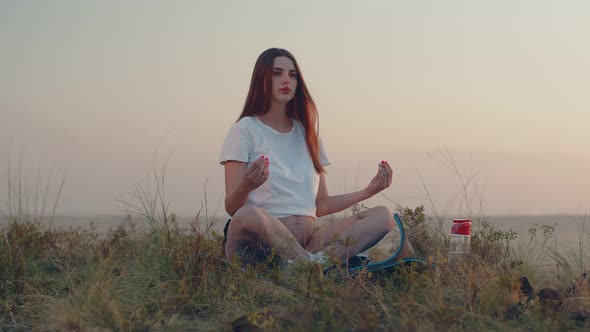 Pregnant Caucasian Woman is Sitting on a Lawn on Mat and Meditating