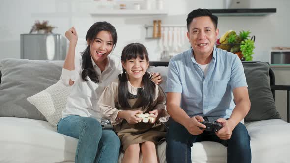 Asian family, father mother and daughter playing console game together in living room at home.