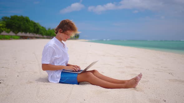 A Student is Engaged in Selfeducation Sitting on the Beach Against the Background of the Turquoise