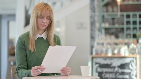 Beautiful Young Woman Reading Documents in Cafe