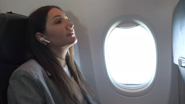 Young Woman Listening to Music with Wireless Headphones on Airplane