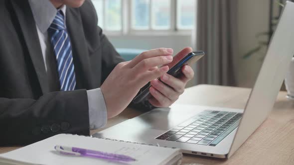 Close Up Of Asian Businessman Using Mobile Phone After Using Computer For Working At Home