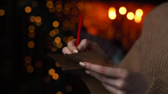 Close-up Hands of Young Woman Writing Christmas Letter To Santa Claus on Background Xmas Tree.