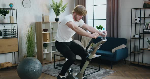 Guy in Sportswear Hard Cycling on Stationary Bike During Morning Home Workout