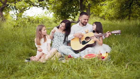 Handsome Man Playing Guitar for His Charming Wife and Two Cute Daughters