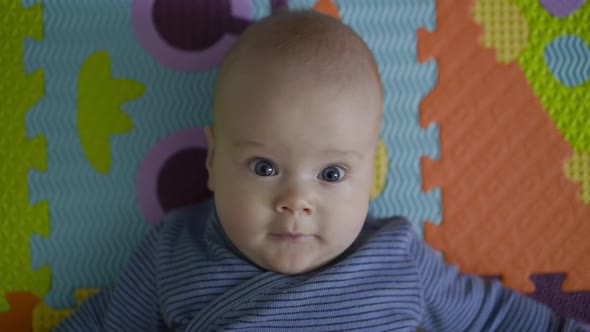 Close View of Cute Newborn with Outstretched Arms Lying on Carpet and Looking