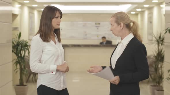 Young Caucasian Brunette Woman Talking Seriously To Mid-adult Employee. Portrait of Confident Female