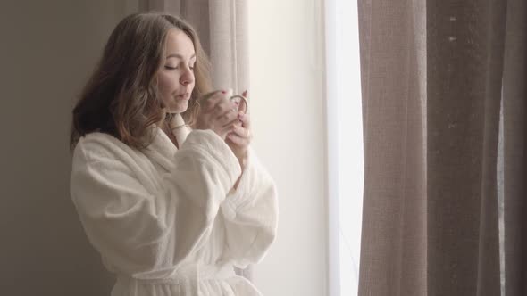 Camera Slowly Approaching Young Brunette Woman Drinking Coffee and Looking Out the Window