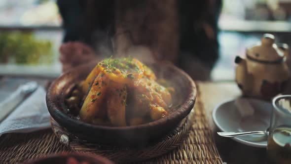 Close up shot of a steaming hot potato dish set in a pottery bowl on a wooden table