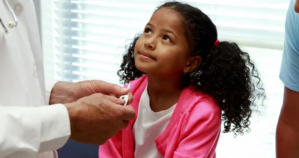 Male doctor interacting with patient while checking temperature on thermometer