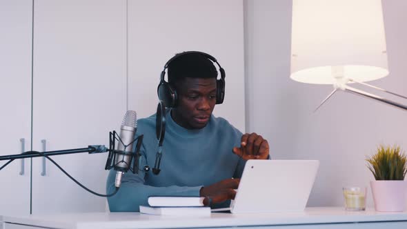 Man Wearing Headphones Doing an Online Meeting Using a Laptop and Microphone