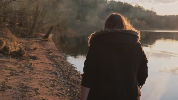 A Woman Walks Along the River Bank on a Cold Autumn Day in the Warm Autumn Sun