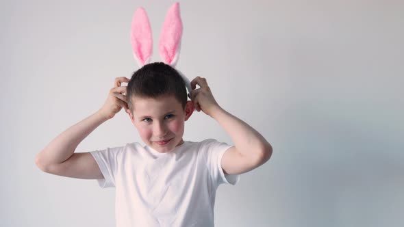 Funny playful boy is wearing bunny ears and white t shirt on background of white wall during Easter
