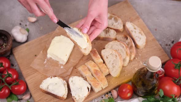 Woman Smearing Soft Butter on Slice of Baguette Bread By Knife at Domestic Kitchen