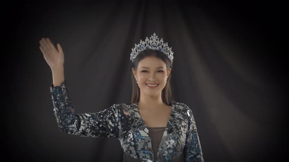 Miss beauty pageant winner wearing her crown stands in the spotlight and waves and blows a kiss